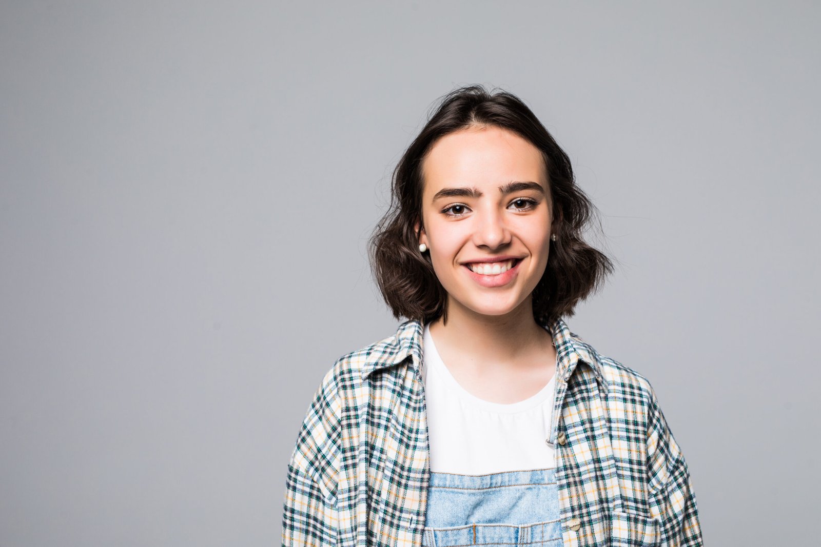 Close up portrait of young cheerful beautiful girl with dark long hair in casual gray shirt smiling with teeth, looking in camera with happy and relaxed face expression, posing for university photo.